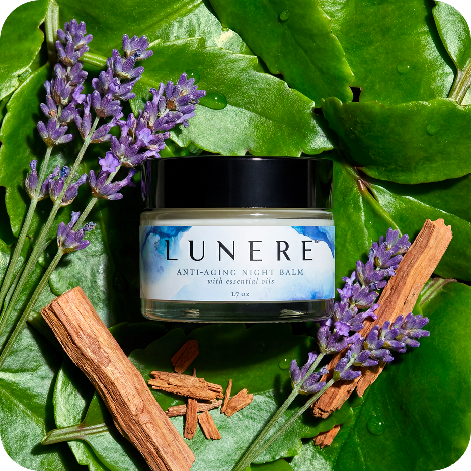 Lunere anti-aging night balm jar surrounded by lavender flowers and sticks on green leaves